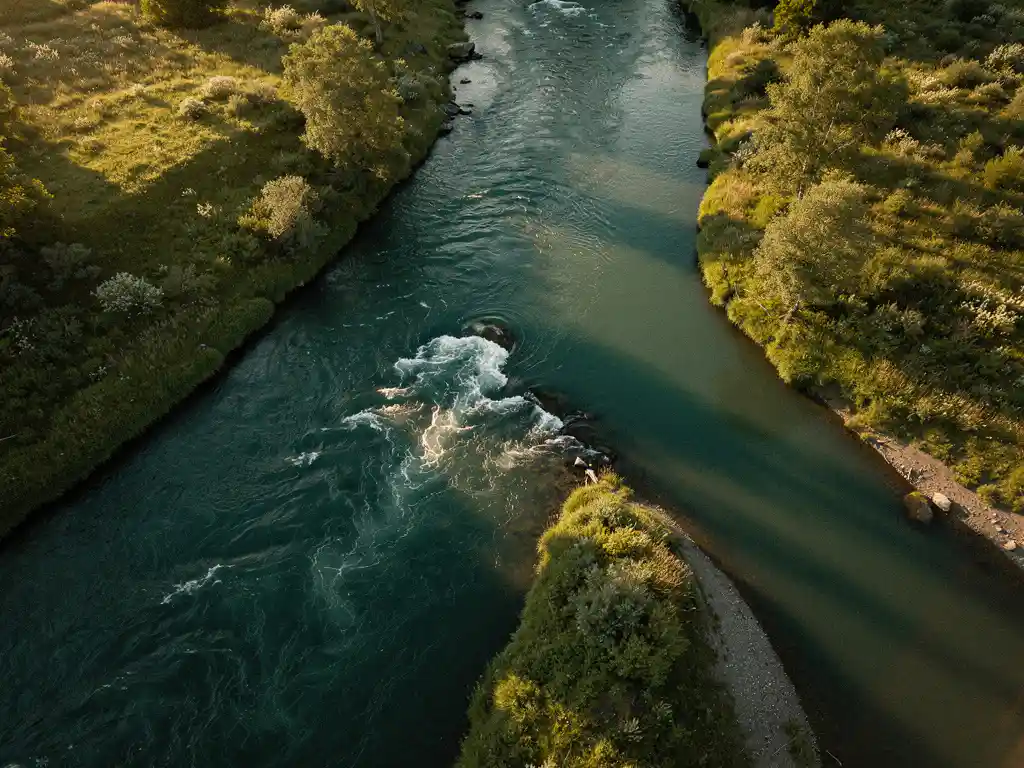 Aerial view of a river splitting into a wide rushing channel and narrow tributary through lush green banks, lit by warm golden sunlight.