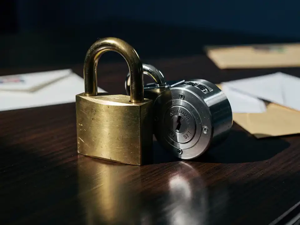 Brass padlock and steel combination lock overlapping on a dark oak desk beside scattered envelopes, symbolizing layered security.