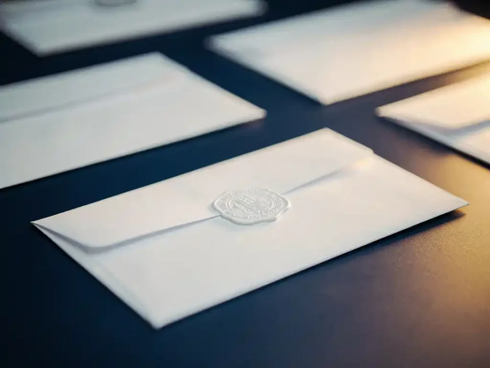 White envelope with a single authentication stamp on a modern desk, blurred duplicate envelopes in the background, navy and amber tones.