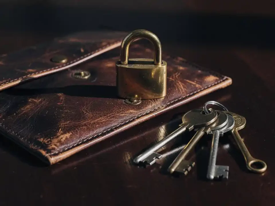 Vintage brass padlock on worn leather envelope flap with three antique keys fanned out on dark mahogany surface.