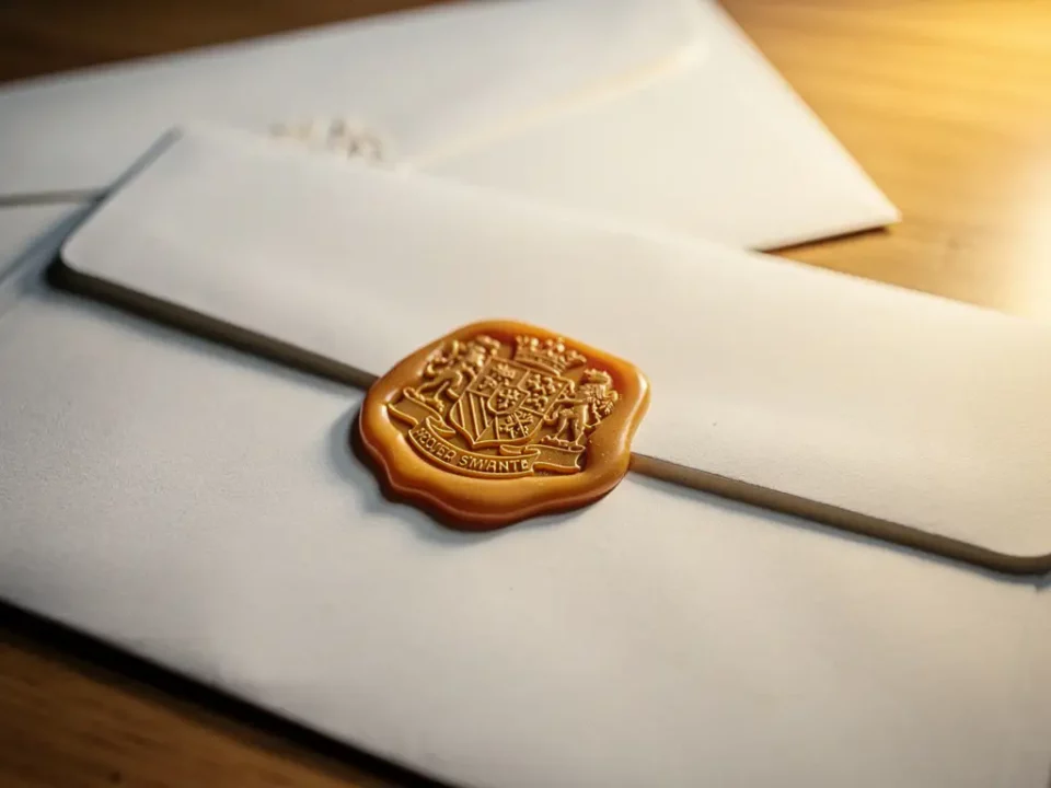 Amber wax seal stamped on a white envelope centered on an oak desk, with soft golden side lighting and shallow depth of field.